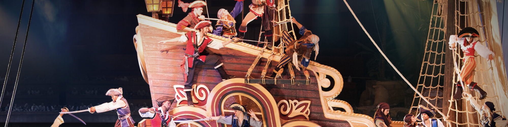 Pirates are performing on a colorful and ornate ship set, featuring action-packed scenes with characters climbing, fighting, and engaging with the audience.